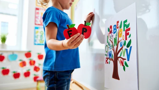 Preschooler matching apple-shaped letter magnets to a tree chart on a whiteboard, apple crafts for preschoolers alphabet activity