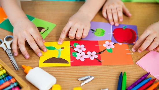 Apple lifecycle craft for preschoolers showing hands assembling a colorful mini book with each stage of the apple life cycle