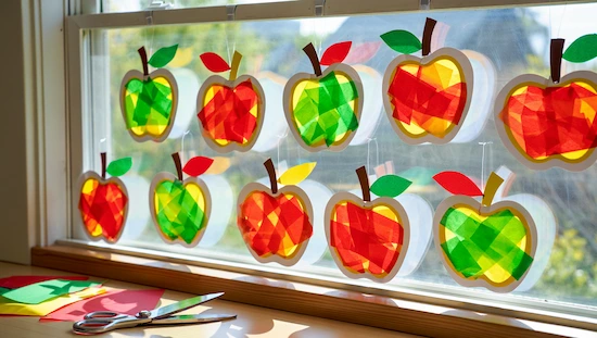 Apple crafts for preschoolers—colorful apple suncatchers made with tissue paper, sunlight shining through classroom window display.