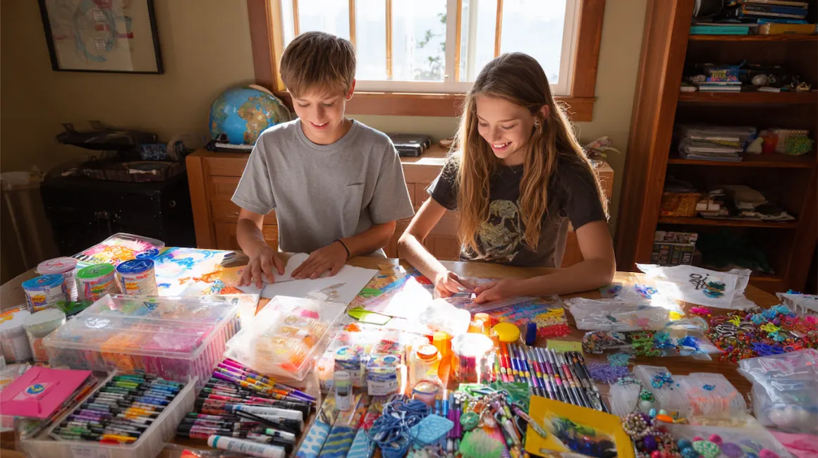 Two tweens working together on creative projects for tweens, surrounded by colorful art supplies and DIY materials at a sunlit craft table.