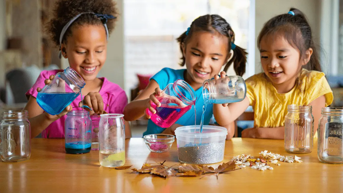 Three children happily creating diy potions for kids using colorful liquids, jars, and natural materials for a playful science project.
