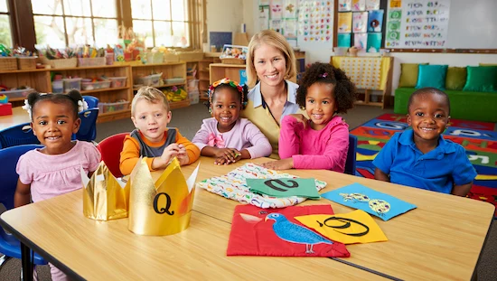 Smiling preschoolers and teacher with letter q crafts for preschoolers—colorful crowns and quilts—in a bright, engaging classroom setting.