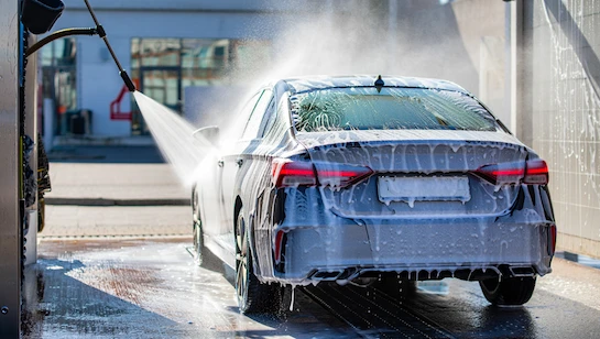 Self-service DIY car wash near me with a car being rinsed under high-pressure water and foam, showing a clean and efficient washing process.