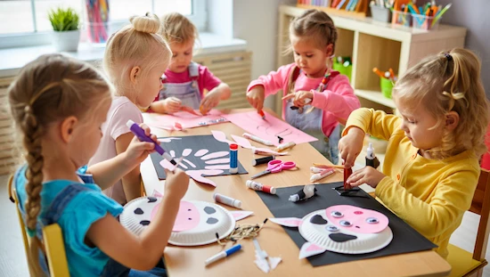 Children creating a cow preschool craft with paper plates and handprint art in a colorful classroom setting.