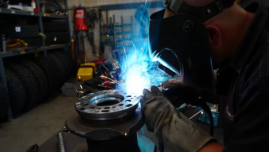Person welding a beadlock ring onto a wheel in a workshop, sparks flying, weld-on diy beadlocks process