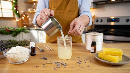 How to make advent candles at home with advent candle DIY—pouring melted wax into a jar, surrounded by natural supplies and festive decor