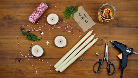 Essential materials for advent candle holder diy, including candles, wooden bases, twine, dried oranges, scissors, and hot glue gun.