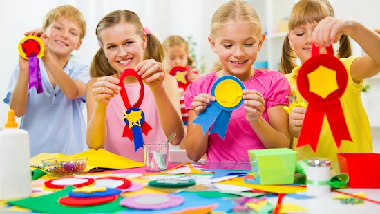 Blonde children happily creating handmade medals and ribbons at a craft table, surrounded by colorful felt, paper, and award diy supplies

