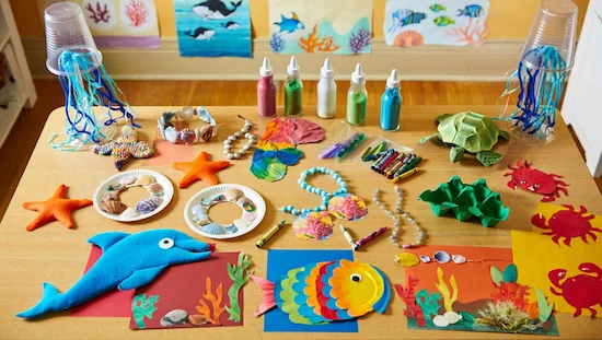 Table with ocean crafts for preschoolers—starfish, fish, turtles, jellyfish, shells, and crabs, all bright and colorful.