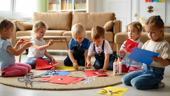 Preschool children making spider craft preschool projects on a rug in a cozy, sunlit living room