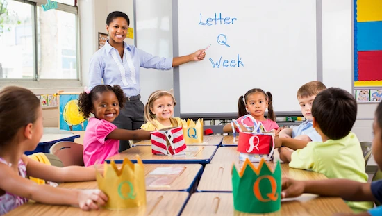 Teacher and students in a classroom with letter q crafts for preschoolers during Letter Q Week, showing crowns and engaged early learners.