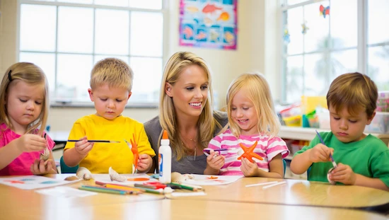 Teacher and kids making ocean crafts for preschoolers, painting shells and starfish in a bright classroom.