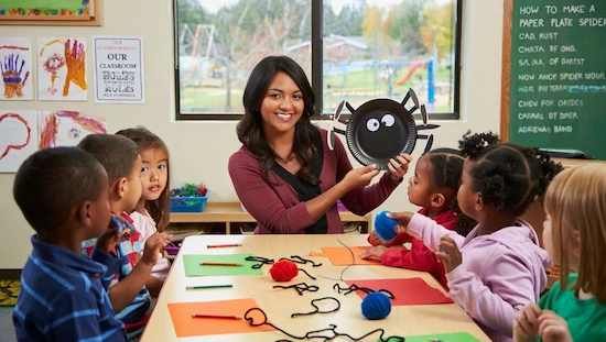 Preschool teacher with children showing spider craft preschool project in a real classroom setting