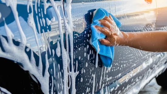 Close-up of a hand wiping a soapy car with a blue microfiber towel at a DIY car wash, showing a clean and shiny finish during the wash process.