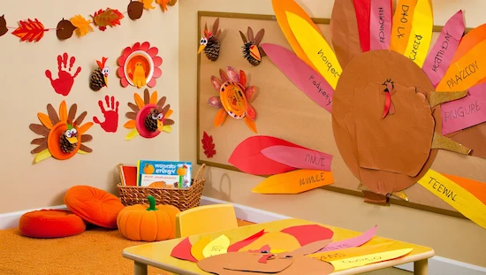 Preschool classroom decorated for Thanksgiving with turkey crafts, handprints, a collaborative mural, fall books, pumpkins, and activity table