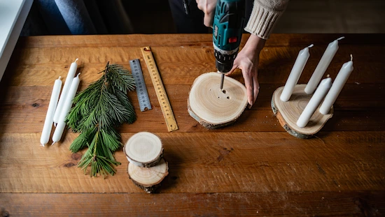 Making an advent candle holder diy using wood slices, drill, taper candles, pine branches, and rulers on a wooden table step-by-step.

