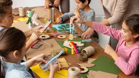 Children and adults making eco-friendly award diy medals and trophies at a craft table using recycled cardboard, wood slices, twine, and natural materials

