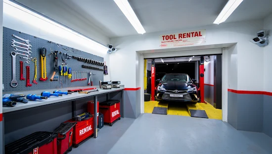 Essential tools and equipment neatly organized on a workbench and tool wall at a diy auto garage rental near me, with a car on a lift in a bright, modern rental garage bay.
