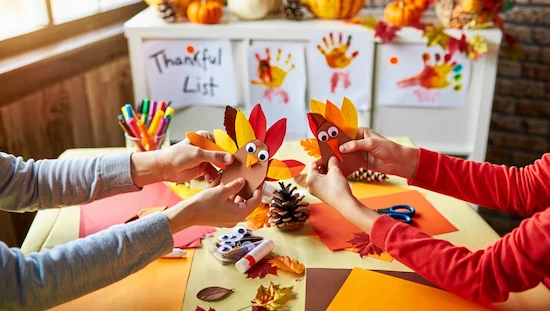 Parent and child hands making turkey crafts preschool project at home, with art supplies, pinecones, and a Thankful List in a sunlit room