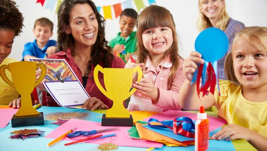 Children and adults smiling while making colorful award diy trophies, ribbons, and certificates at a festive table with craft supplies and decorations

