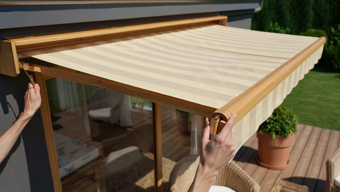 Hands adjusting diy awning with wood frame and beige fabric, installed over patio door, offering adjustable shade outdoors.