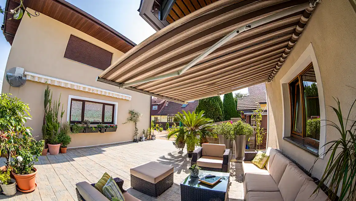 DIY Awning Ideas feature image: stylish patio with retractable striped awning, window awning, lush greenery, and outdoor seating area.