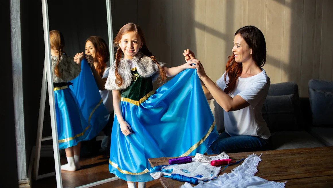 Mother helping daughter with anna frozen costume diy, finishing dress details, sewing, and enjoying a creative bonding moment at home.