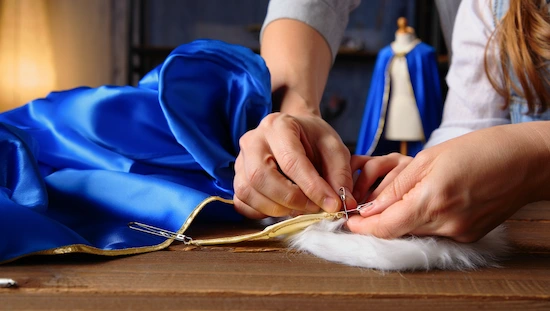 Close-up of hands sewing blue and gold fabric for anna frozen costume diy, showing detail and care in creating a unique costume.