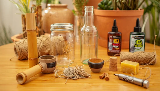 Eco-friendly DIY bong kit made with bamboo, mason jar, glass bottle, twine, corks, ceramic bowls, and upcycling tools on a table.