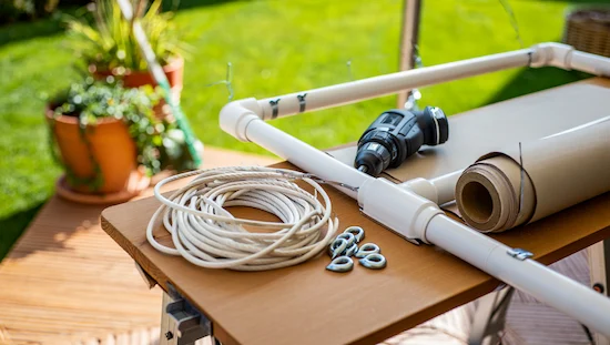 DIY awning retractable build in progress, showing PVC frame, outdoor fabric, ropes, drill, and hardware for homemade shade project.