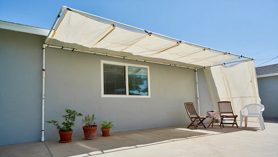 A backyard setup with a PVC and canvas drop cloth awning, featuring simple seating and plants, cheap diy awning ideas in action.