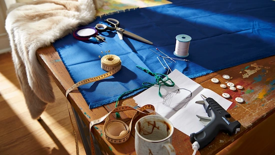 Sewing supplies, fabric, thread, glue gun, and fur displayed on a table, ready for an anna frozen costume diy craft project.