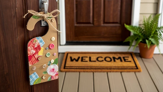 Homemade door hanger diy made from recycled cardboard, colorful fabric pieces, and buttons, hanging on a cozy front door.

