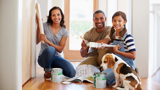Family with natural skin tones doing diy door trim molding together, painting trim, using eco-friendly paint, and smiling with their dog.