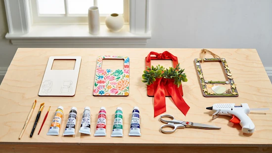 Step-by-step diy door hanger process showing sketching, painting, decorating, and finishing with tools, paints, and greenery on a table.

