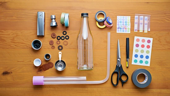 Affordable DIY bong kit parts with bottle, tubing, washers, tape, scissors, stickers, and tools arranged for budget-friendly crafting.