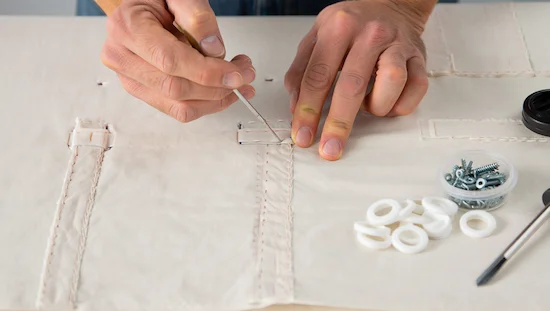 Close-up of hands sewing pocket pieces on fabric and prepping #8 eye screws and slip-on caps for a diy retractable awning project