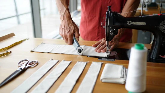 Person cutting and sewing sailcloth panels and pockets with a rotary cutter and sewing machine for strong DIY awning ideas shade.