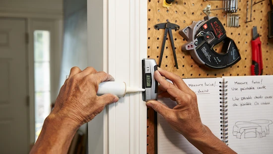 Hands applying caulk to diy door trim with measuring tools, notebook, and pro tips in a well-equipped home workshop.

