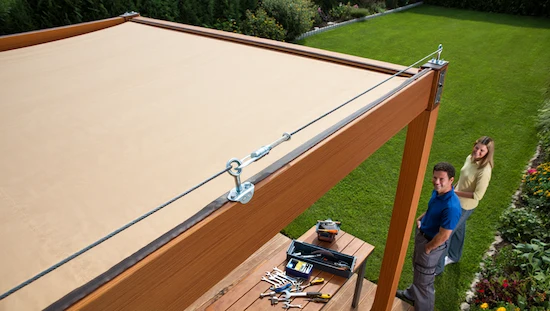 DIY retractable awning installed over a patio, taut sailcloth canopy, secure cables, smiling couple, lush garden, tools put away