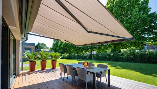Modern retractable awning for deck shading a dining table and chairs, with potted plants and a sunny backyard in the background.